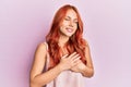 Young beautiful redhead woman wearing casual clothes over pink background smiling with hands on chest, eyes closed with grateful Royalty Free Stock Photo