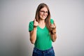 Young beautiful redhead woman wearing casual green t-shirt and glasses over white background doing money gesture with hands, Royalty Free Stock Photo