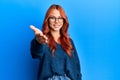 Young beautiful redhead woman wearing casual sweater and glasses over blue background smiling friendly offering handshake as Royalty Free Stock Photo