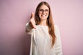 Young beautiful redhead woman wearing casual sweater and glasses over pink background smiling friendly offering handshake as Royalty Free Stock Photo