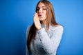 Young beautiful redhead woman wearing casual sweater over isolated blue background hand on mouth telling secret rumor, whispering Royalty Free Stock Photo