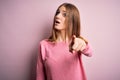 Young beautiful redhead woman wearing casual sweater over isolated pink background pointing displeased and frustrated to the Royalty Free Stock Photo