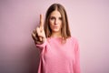 Young beautiful redhead woman wearing casual sweater over isolated pink background Pointing with finger up and angry expression, Royalty Free Stock Photo