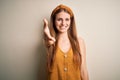 Young beautiful redhead woman wearing casual t-shirt and diadem over yellow background smiling friendly offering handshake as Royalty Free Stock Photo