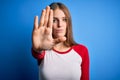 Young beautiful redhead woman wearing casual t-shirt over isolated blue background doing stop sing with palm of the hand Royalty Free Stock Photo