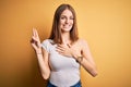 Young beautiful redhead woman wearing casual t-shirt over  yellow background smiling swearing with hand on chest and Royalty Free Stock Photo