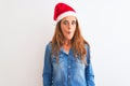 Young beautiful redhead woman wearing christmas hat over isolated background making fish face with lips, crazy and comical gesture Royalty Free Stock Photo