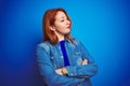 Young beautiful redhead woman wearing denim shirt standing over blue isolated background looking to the side with arms crossed Royalty Free Stock Photo