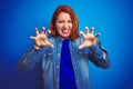 Young beautiful redhead woman wearing denim shirt standing over blue isolated background smiling funny doing claw gesture as cat, Royalty Free Stock Photo