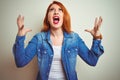 Young beautiful redhead woman wearing denim shirt standing over white isolated background crazy and mad shouting and yelling with Royalty Free Stock Photo