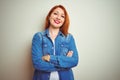 Young beautiful redhead woman wearing denim shirt standing over white isolated background happy face smiling with crossed arms Royalty Free Stock Photo