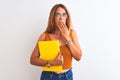 Young beautiful redhead woman wearing glasses reading a book over isolated background cover mouth with hand shocked with shame for Royalty Free Stock Photo