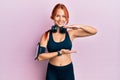 Young beautiful redhead woman wearing gym clothes and using headphones gesturing with hands showing big and large size sign, Royalty Free Stock Photo