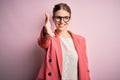 Young beautiful redhead woman wearing jacket and glasses over isolated pink background smiling friendly offering handshake as Royalty Free Stock Photo