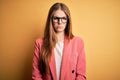 Young beautiful redhead woman wearing jacket and glasses over isolated yellow background skeptic and nervous, frowning upset Royalty Free Stock Photo
