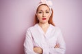 Young beautiful redhead woman wearing pajama standing over pink isolated background with serious expression on face Royalty Free Stock Photo