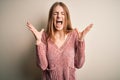 Young beautiful redhead woman wearing pink casual sweater over isolated white background celebrating mad and crazy for success Royalty Free Stock Photo