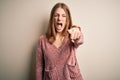 Young beautiful redhead woman wearing pink casual sweater over isolated white background pointing displeased and frustrated to the Royalty Free Stock Photo