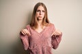 Young beautiful redhead woman wearing pink casual sweater over isolated white background Pointing down looking sad and upset, Royalty Free Stock Photo