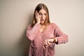 Young beautiful redhead woman wearing pink casual sweater over white background Looking at the watch time worried, afraid