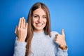 Young beautiful redhead woman wearing wedding ring on finger over blue background happy with big smile doing ok sign, thumb up