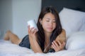 Young beautiful Asian Chinese woman with earpiece listening to music smiling happy lying on bed using internet on mobile phone Royalty Free Stock Photo