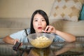 Young beautiful and relaxed Asian Chinese woman watching Korean drama on television on sad romantic movie eating popcorn at home Royalty Free Stock Photo