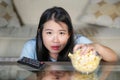 Young beautiful and relaxed Asian Chinese woman watching Korean drama on television on sad romantic movie eating popcorn at home Royalty Free Stock Photo