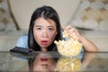 Young beautiful and relaxed Asian Japanese woman watching Korean drama on television on sad romantic movie eating popcorn at home Royalty Free Stock Photo