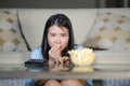 Young beautiful and relaxed Asian Japanese woman watching Korean drama on television on sad romantic movie eating popcorn at home Royalty Free Stock Photo