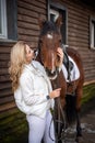 Young beautiful rider woman blonde with long hair in white clothes standing near horse on farm Royalty Free Stock Photo