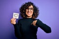 Young beautiful romantic arab woman wearing glasses holding reminder paper with heart with surprise face pointing finger to