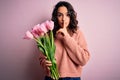 Young beautiful romantic woman with curly hair holding bouquet of pink tulips asking to be quiet with finger on lips Royalty Free Stock Photo