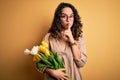 Young beautiful romantic woman with curly hair holding bouquet of yellow tulips asking to be quiet with finger on lips Royalty Free Stock Photo