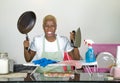 Young beautiful sad and desperate black African American woman stressed working frustrated at home kitchen with pan and iron in do