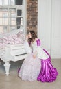 Young beautiful sad woman in fantasy rococo style medieval dress sitting near piano with pink flowers Royalty Free Stock Photo