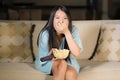 Young beautiful and scared Asian Chinese teenager woman in fear watching horror scary movie at home sofa couch eating popcorn bowl Royalty Free Stock Photo