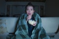 Young beautiful scared and frightened Asian Chinese woman watching horror scary movie or thriller eating popcorn in fear face Royalty Free Stock Photo