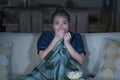 Young beautiful scared and frightened Asian Chinese woman watching horror scary movie or thriller eating popcorn in fear face