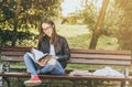 Young beautiful school or college girl with glasses sitting on the bench in the park reading the books and study for exam