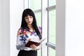 Young Beautiful serious woman standing near the window, writing in notebook, looking to the notebook Royalty Free Stock Photo