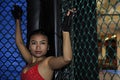 Beautiful and Asian fighter woman in fighting gloves and sport clothes inside MMA cage posing cool