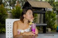 Young beautiful and Asian woman in stylish dress at holiday resort coffee shop or restaurant drinking healthy fruit juice Royalty Free Stock Photo