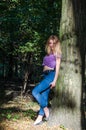 Young beautiful girl blond model with long blond hair in jeans and jacket posing in the woods among the trees and vegetation