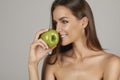 Young beautiful girl with dark curly hair, bare shoulders and neck, holding big green apple to enjoy the taste and are dietin Royalty Free Stock Photo