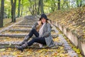 Young beautiful girl model posing in the autumn park among fallen yellow leaves on the old stairs in a hat, coat, jeans and b Royalty Free Stock Photo