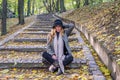 Young beautiful girl model posing in the autumn park among fallen yellow leaves on the old stairs in a hat, coat, jeans and b Royalty Free Stock Photo