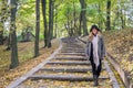 Young beautiful girl model posing in the autumn park among fallen yellow leaves on the old stairs in a hat, coat, jeans and b Royalty Free Stock Photo