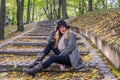 Young beautiful girl model posing in the autumn park among fallen yellow leaves on the old stairs in a hat, coat, jeans and b Royalty Free Stock Photo