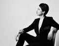 Young beautiful short haired brunette woman in elegant business suit with deep neckline sitting on chair and looking aside Royalty Free Stock Photo